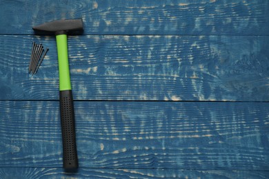 New hammer and metal nails on blue wooden table, flat lay. Space for text