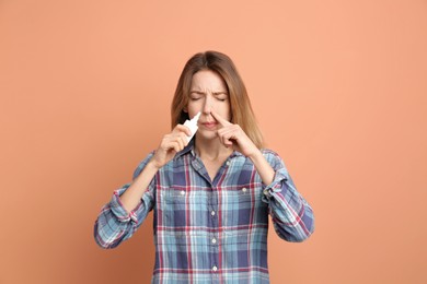 Photo of Sick young woman using nasal spray on coral background