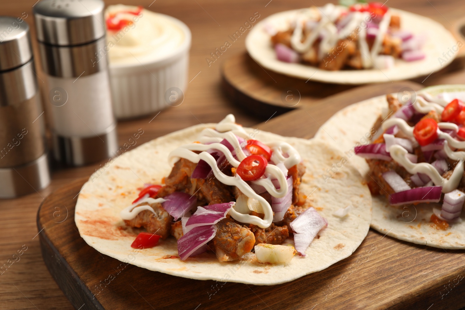 Photo of Delicious tacos with vegetables, meat and sauce on wooden table, closeup