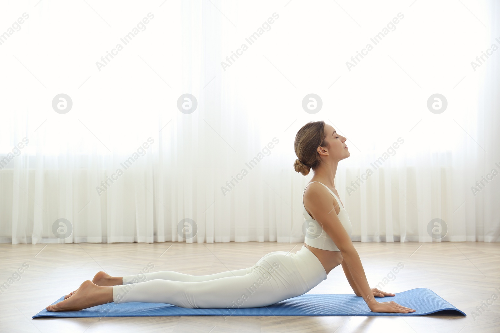 Photo of Young woman practicing high cobra asana in yoga studio. Bhujangasana pose