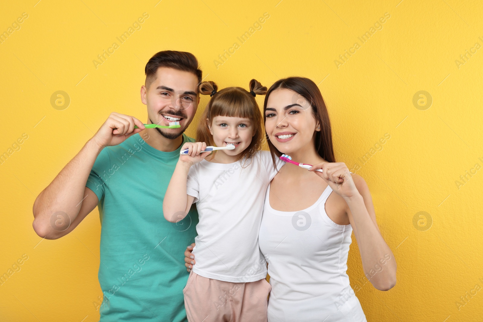 Photo of Little girl and her parents brushing teeth together on color background