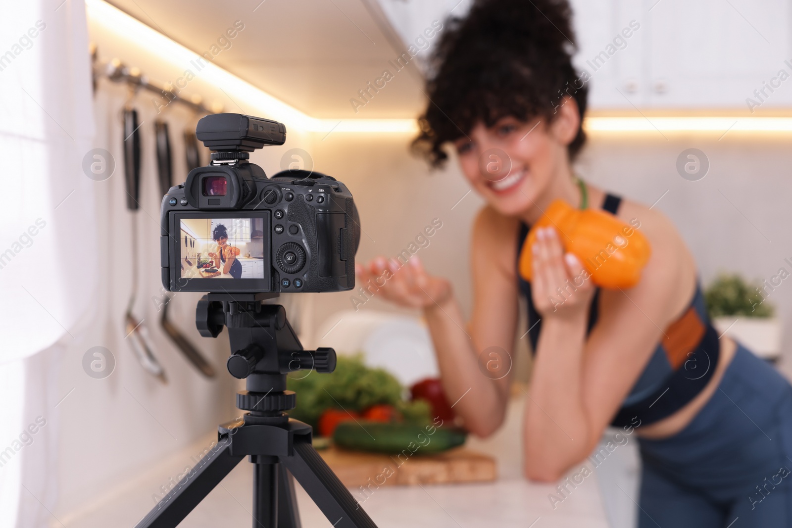 Photo of Food blogger explaining something while recording video in kitchen, focus on camera