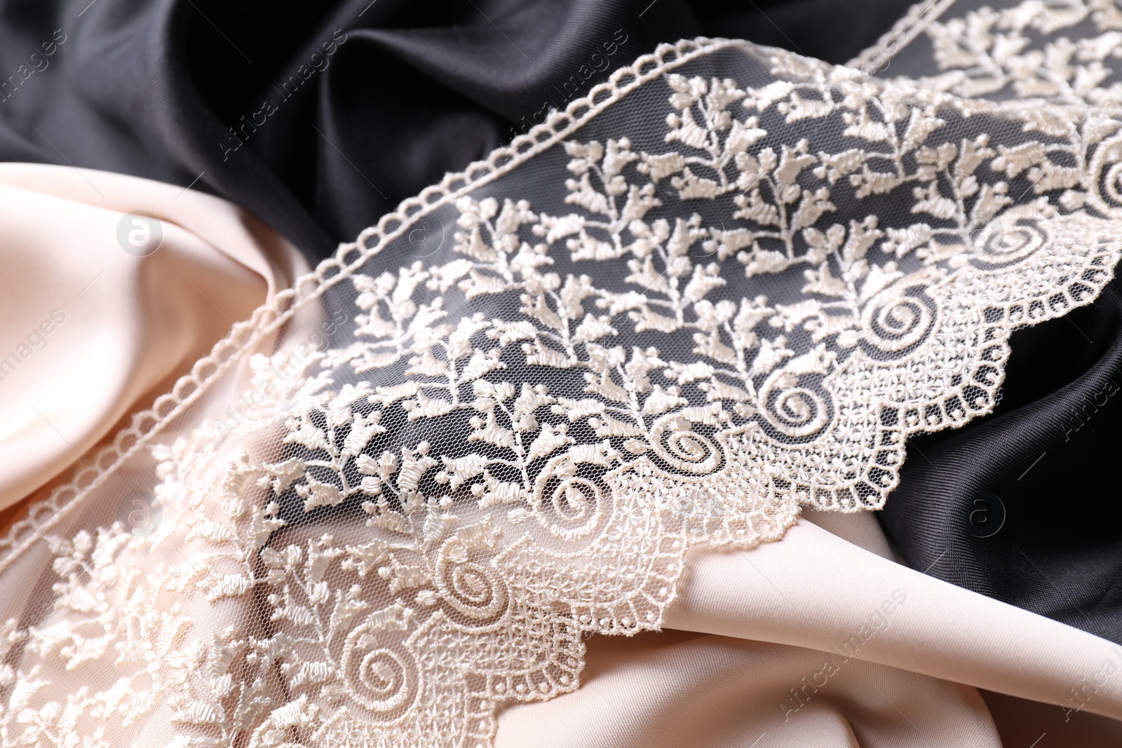 Photo of Beautiful beige lace on color fabrics, closeup