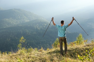 Photo of Man with trekking poles hiking in mountains, back view. Space for text