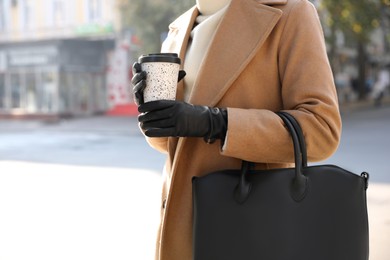 Woman with stylish leather gloves and cup of coffee on city street, closeup