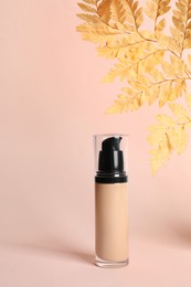 Bottle of skin foundation and decorative plant on beige background. Makeup product
