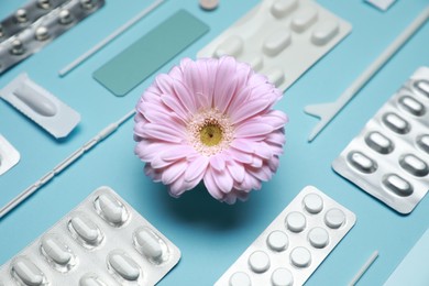 Many gynecological pills, tools and gerbera flower on light blue background, closeup