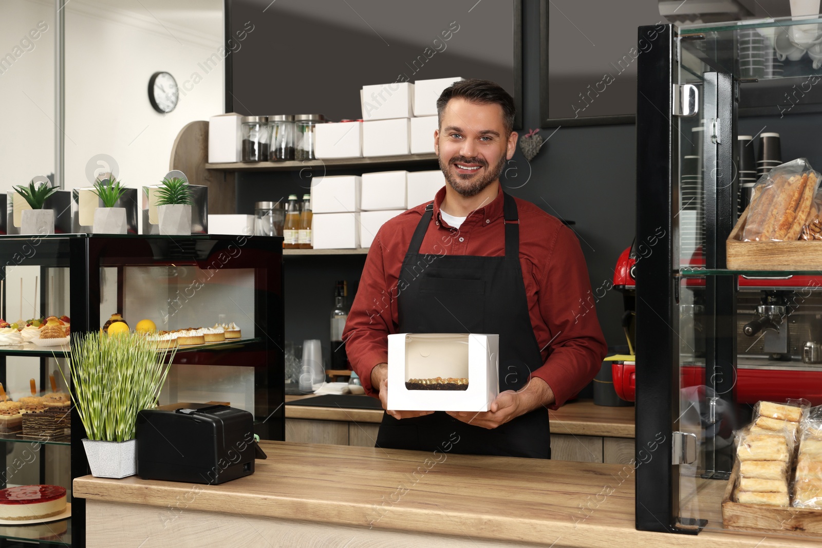 Photo of Business owner in his cafe. Man holding box with cake at desk
