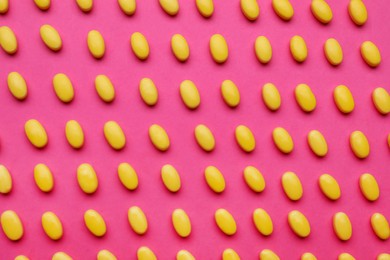 Photo of Many yellow dragee candies on pink background, flat lay
