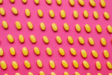 Many yellow dragee candies on pink background, flat lay