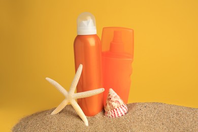 Sand with bottles of sunscreens, starfish and seashell against orange background. Sun protection