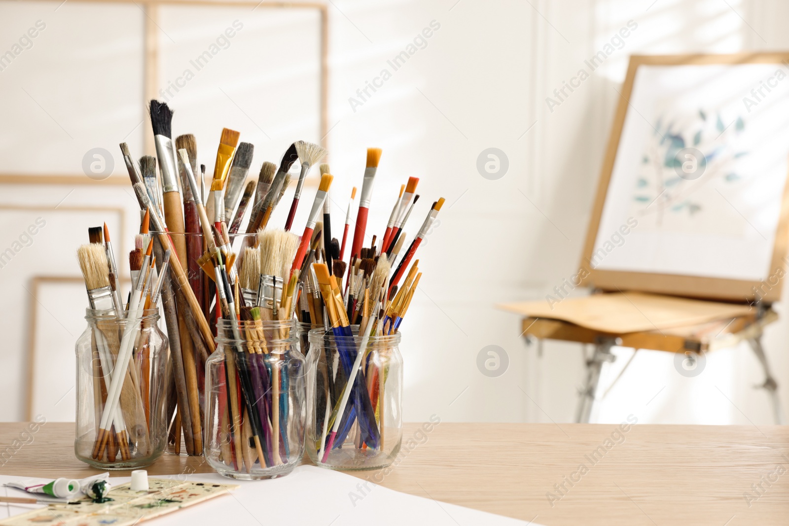 Photo of Holders with different paintbrushes on wooden table in studio, space for text. Artist's workplace