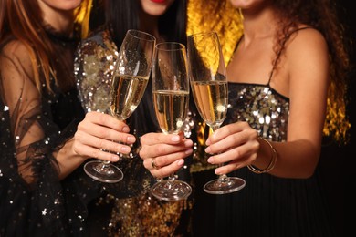 Women with glasses of sparkling wine celebrating New Year on black background, closeup