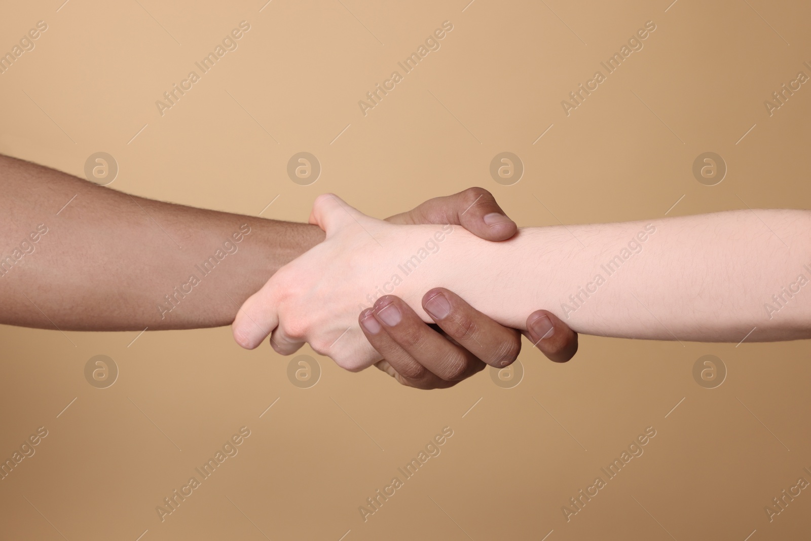 Photo of International relationships. People holding hands on light brown background, closeup