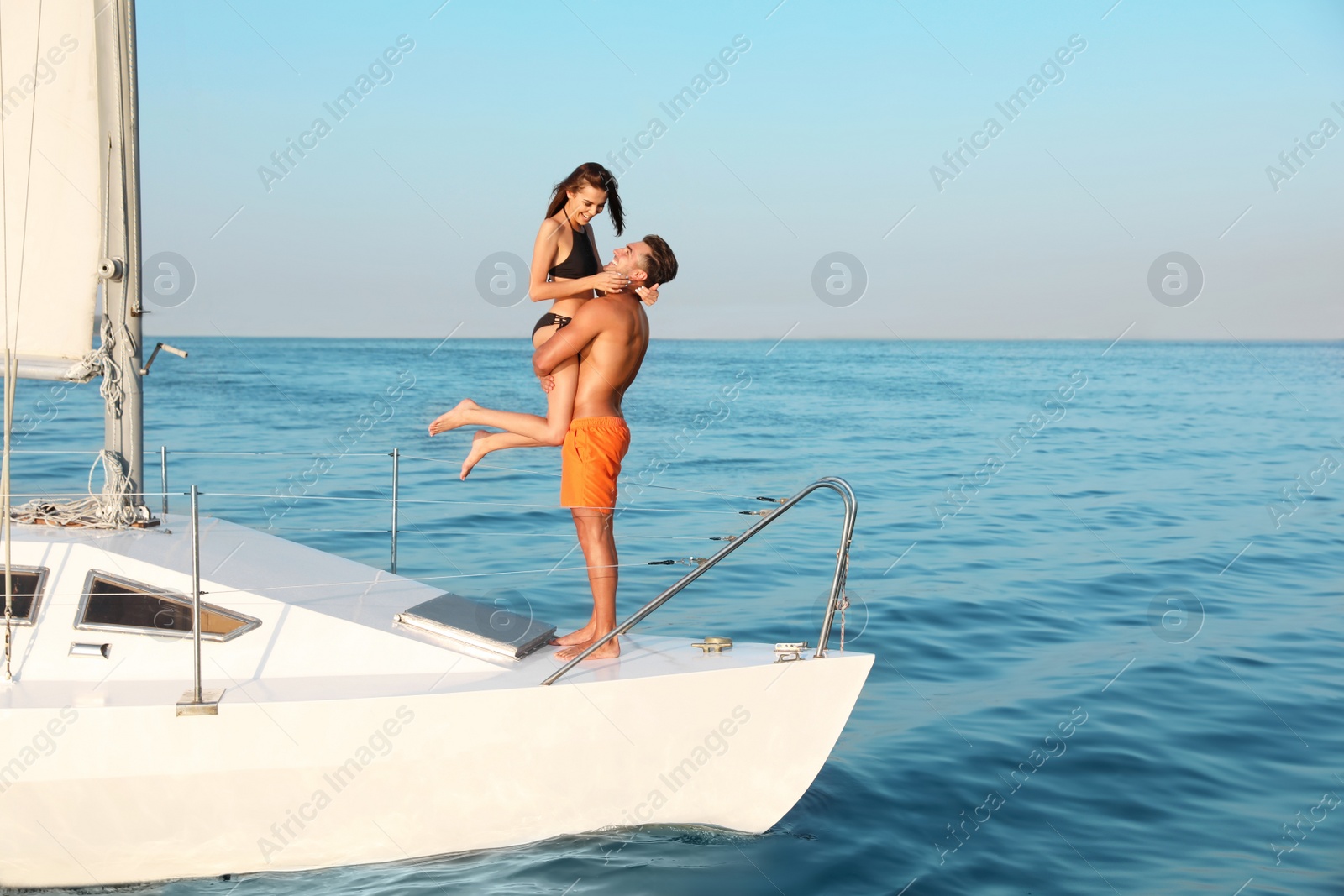 Photo of Young man and his beautiful girlfriend in bikini on yacht. Happy couple during sea trip