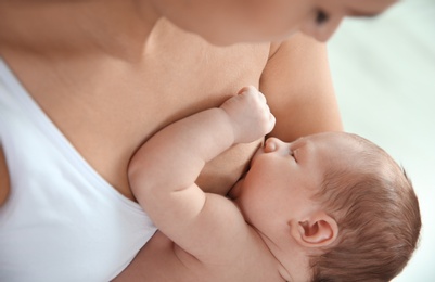 Young woman breastfeeding her baby on light background, closeup