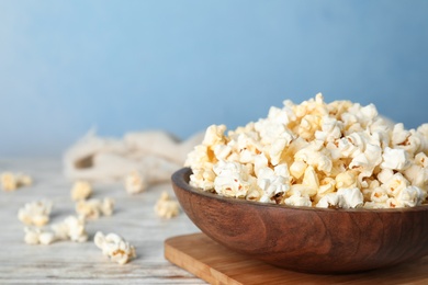 Photo of Wooden bowl with tasty popcorn on table. Space for text