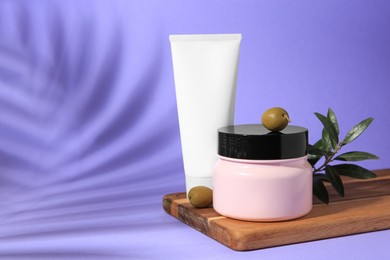 Cosmetic products and olives on lilac background, space for text