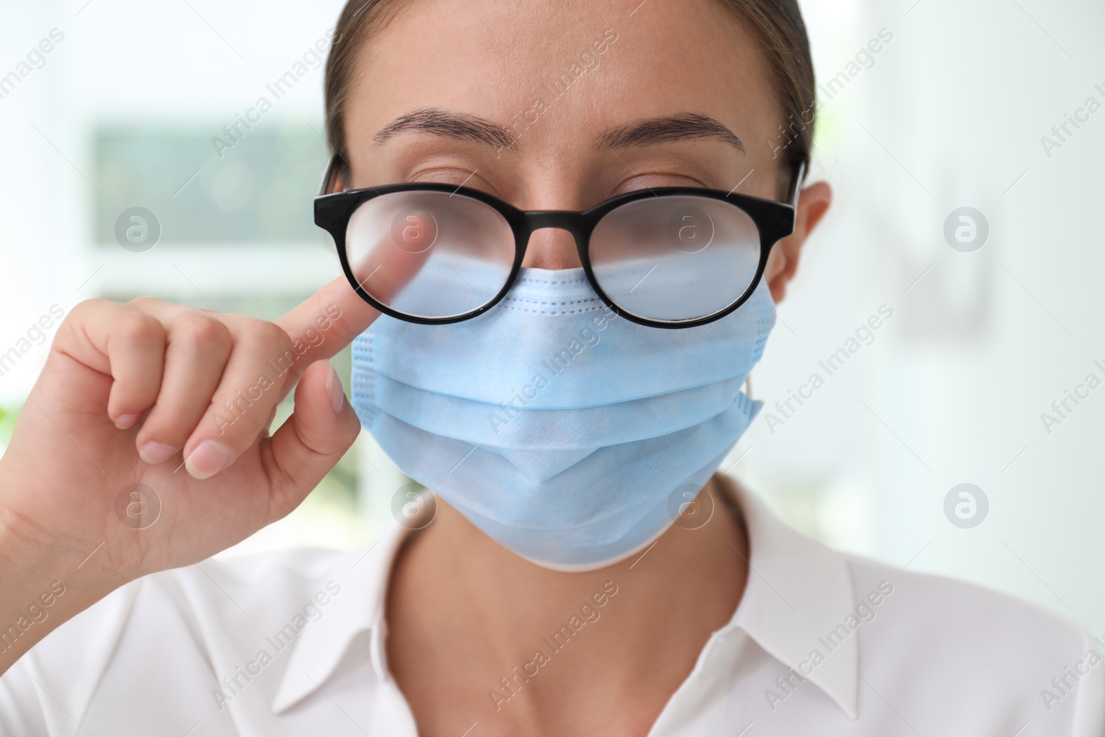 Photo of Woman wiping foggy glasses caused by wearing medical mask indoors, closeup