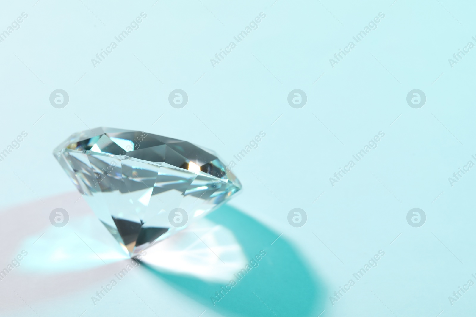 Photo of Beautiful dazzling diamond on turquoise background, closeup. Space for text