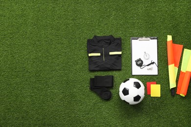 Photo of Uniform, soccer ball and other referee equipment on green grass, flat lay. Space for text