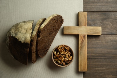 Photo of Bread, walnuts and cross on wooden table, flat lay