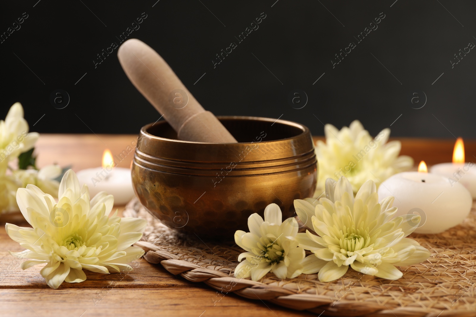 Photo of Tibetan singing bowl with mallet, beautiful chrysanthemum flowers and burning candles on wooden table, closeup