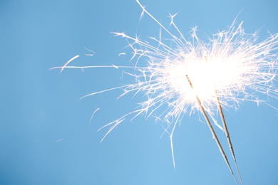 Photo of Bright burning sparklers on light blue background, closeup