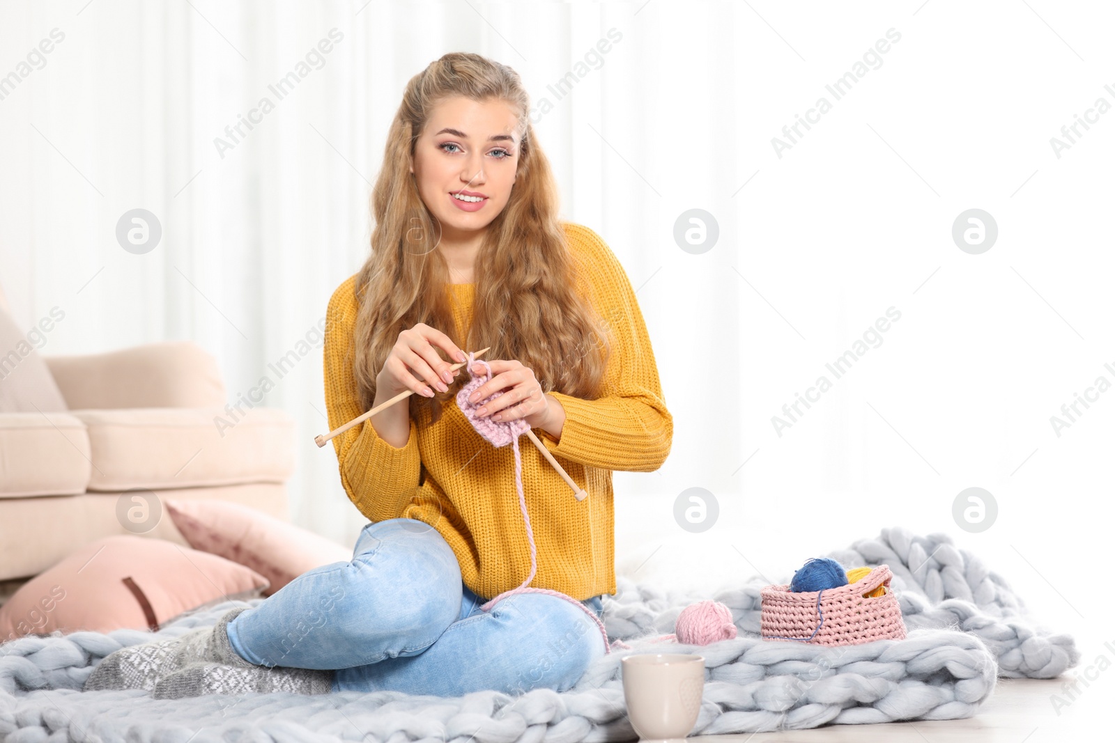 Photo of Young woman in cozy warm sweater knitting with needles on floor at home. Space for text