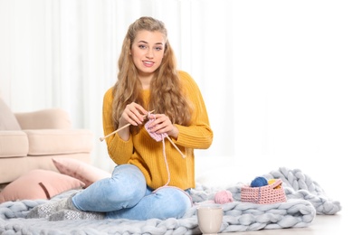 Photo of Young woman in cozy warm sweater knitting with needles on floor at home. Space for text