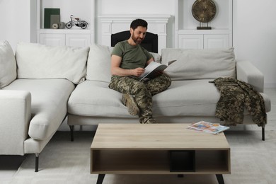 Happy soldier reading magazine on sofa in living room. Military service