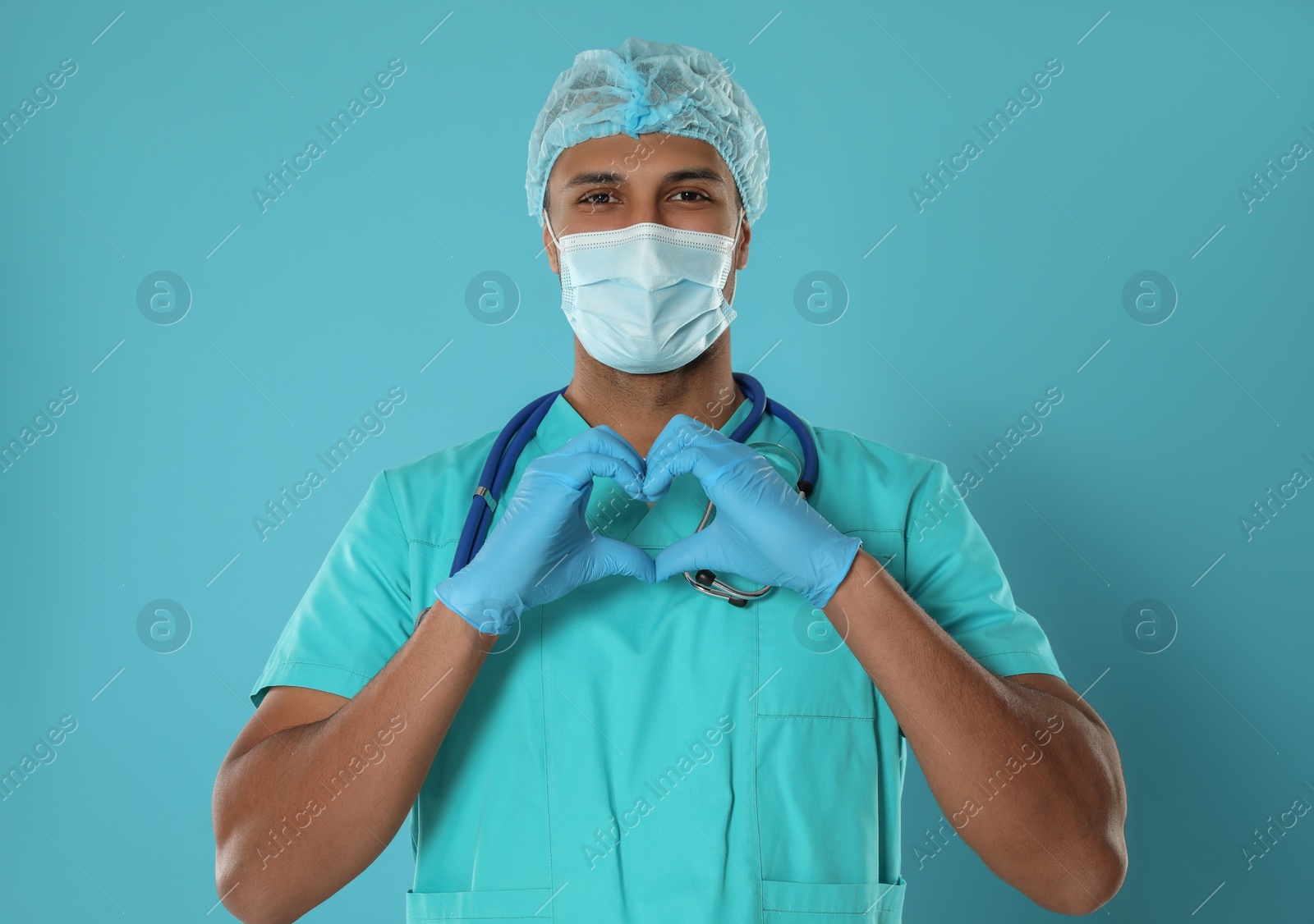 Photo of Doctor or medical assistant (male nurse) with protective mask and stethoscope making heart on turquoise background