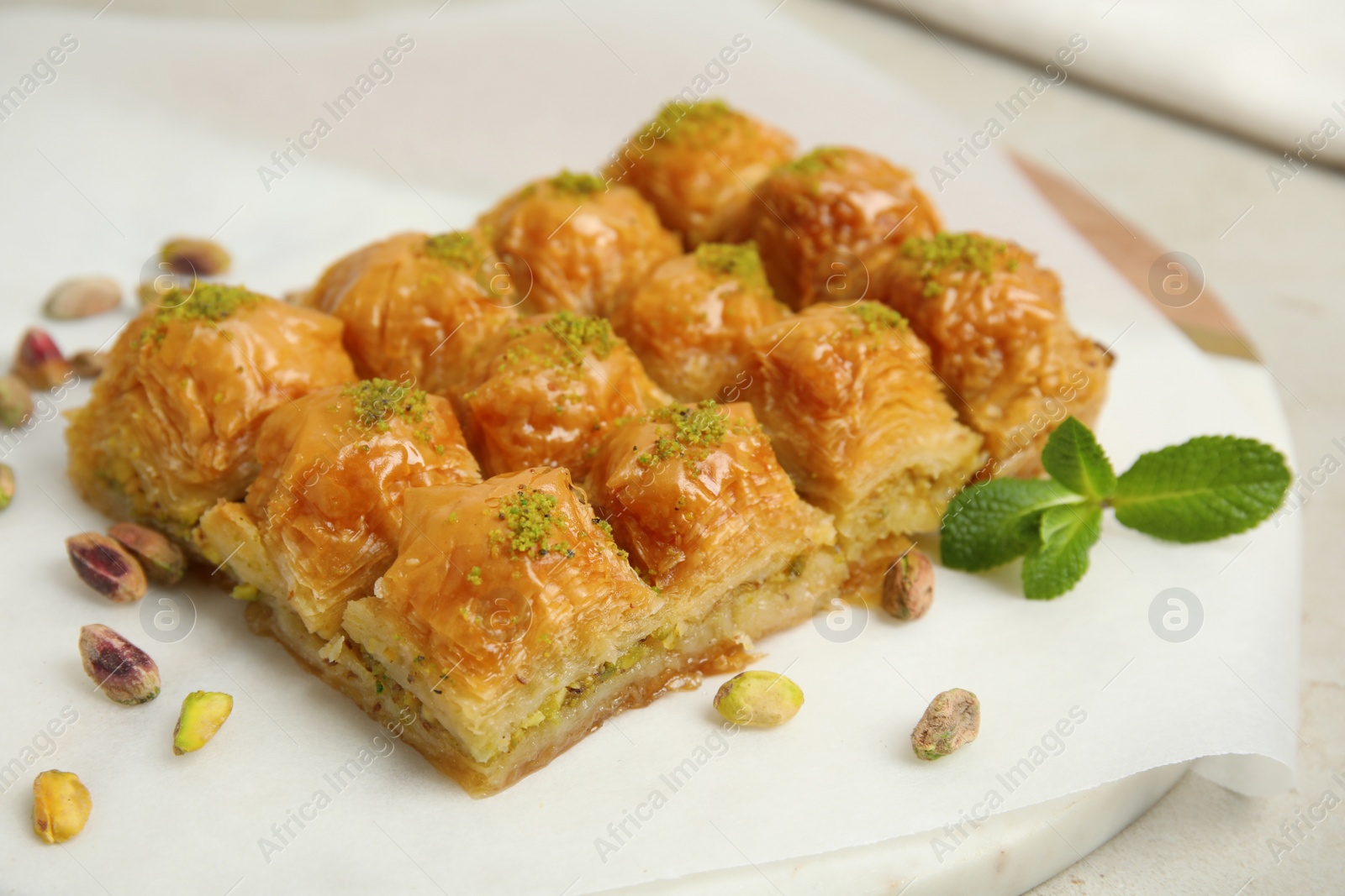 Photo of Delicious sweet baklava with pistachios and mint on board, closeup