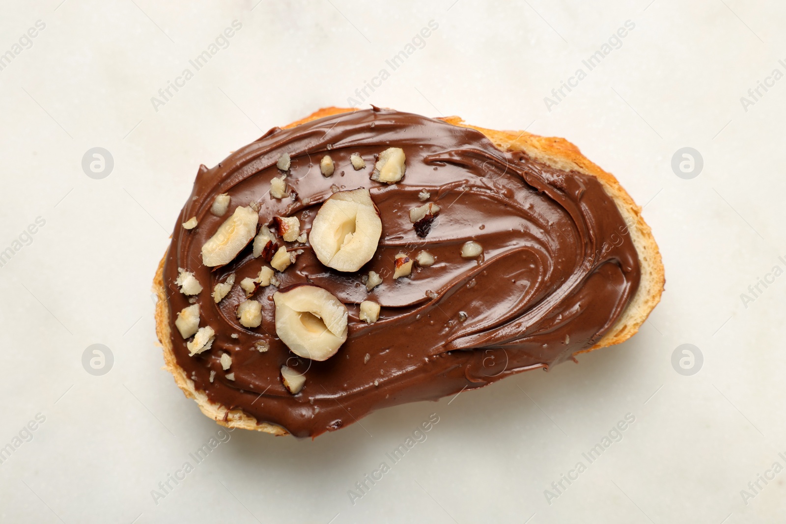 Photo of Slice of bread with tasty chocolate hazelnut spread on white background, top view