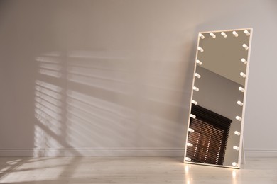 Stylish mirror with light bulbs near white wall indoors. Interior element