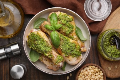 Photo of Delicious fried chicken drumsticks with pesto sauce and ingredients on wooden table, flat lay