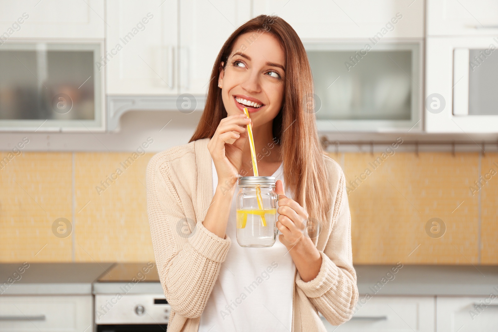 Photo of Young woman drinking lemon water in kitchen