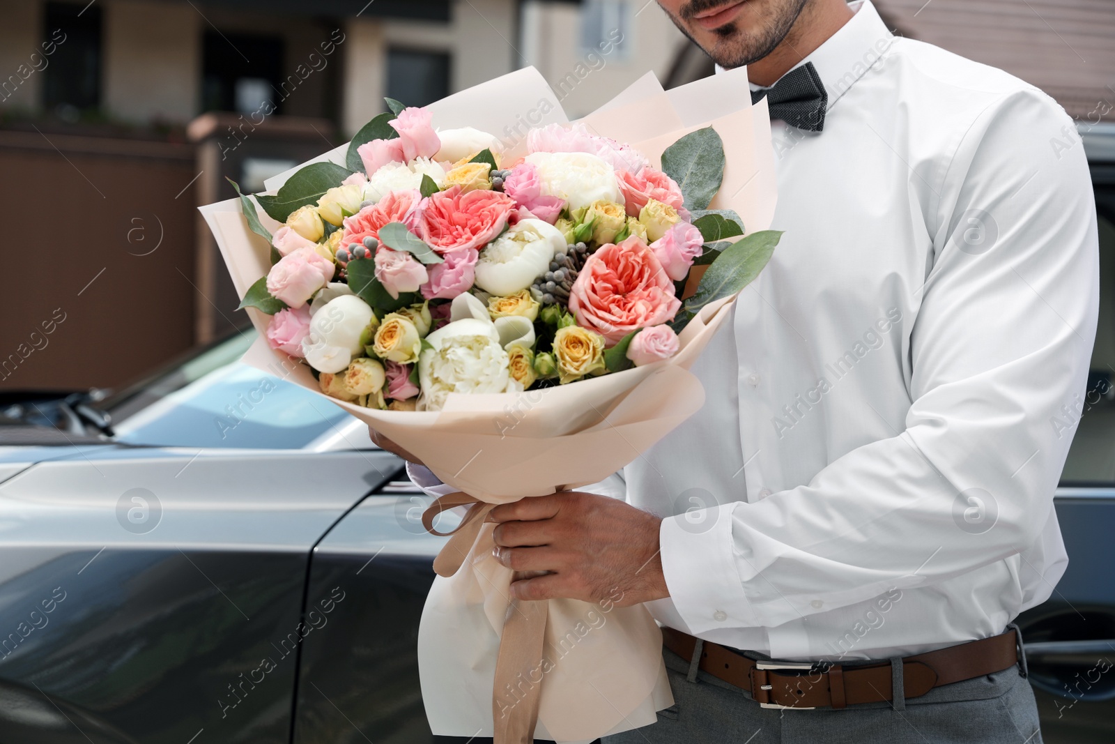 Photo of Young handsome man with beautiful flower bouquet near car outdoors, closeup view