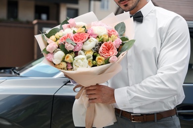 Young handsome man with beautiful flower bouquet near car outdoors, closeup view