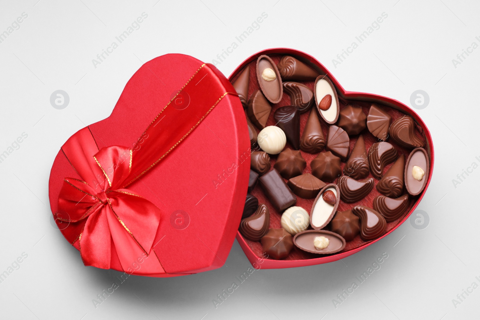 Photo of Heart shaped box with delicious chocolate candies on white background, top view