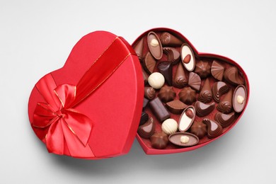 Heart shaped box with delicious chocolate candies on white background, top view