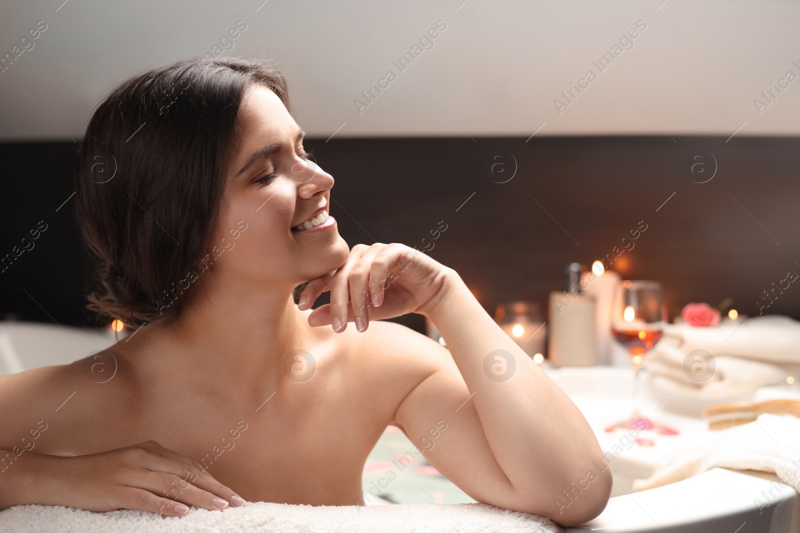 Photo of Happy beautiful woman taking bath with flower petals indoors. Romantic atmosphere