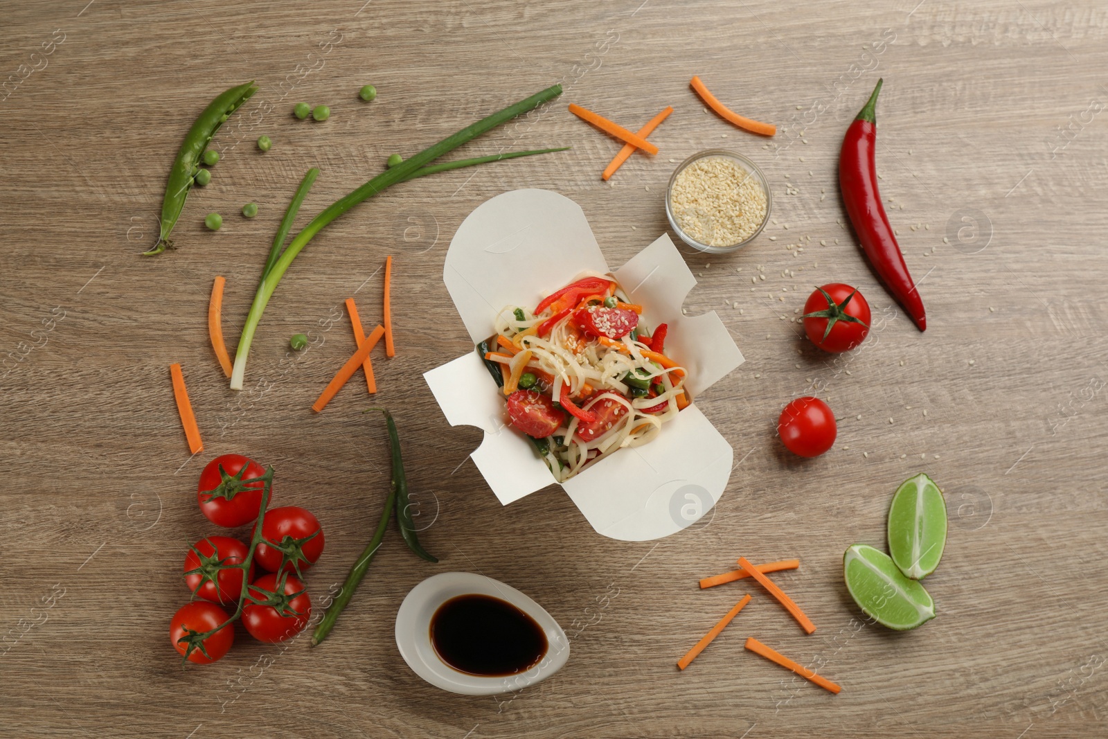 Photo of Box of vegetarian wok noodles with ingredients on wooden table, flat lay