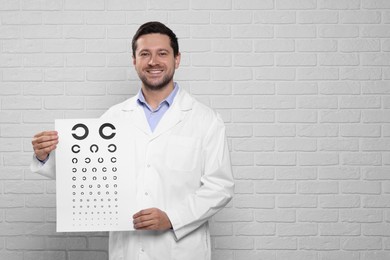 Ophthalmologist with vision test chart near white brick wall, space for text