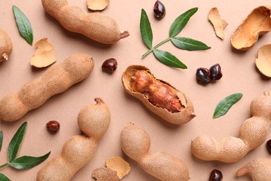 Photo of Ripe tamarinds and fresh leaves on beige background, flat lay