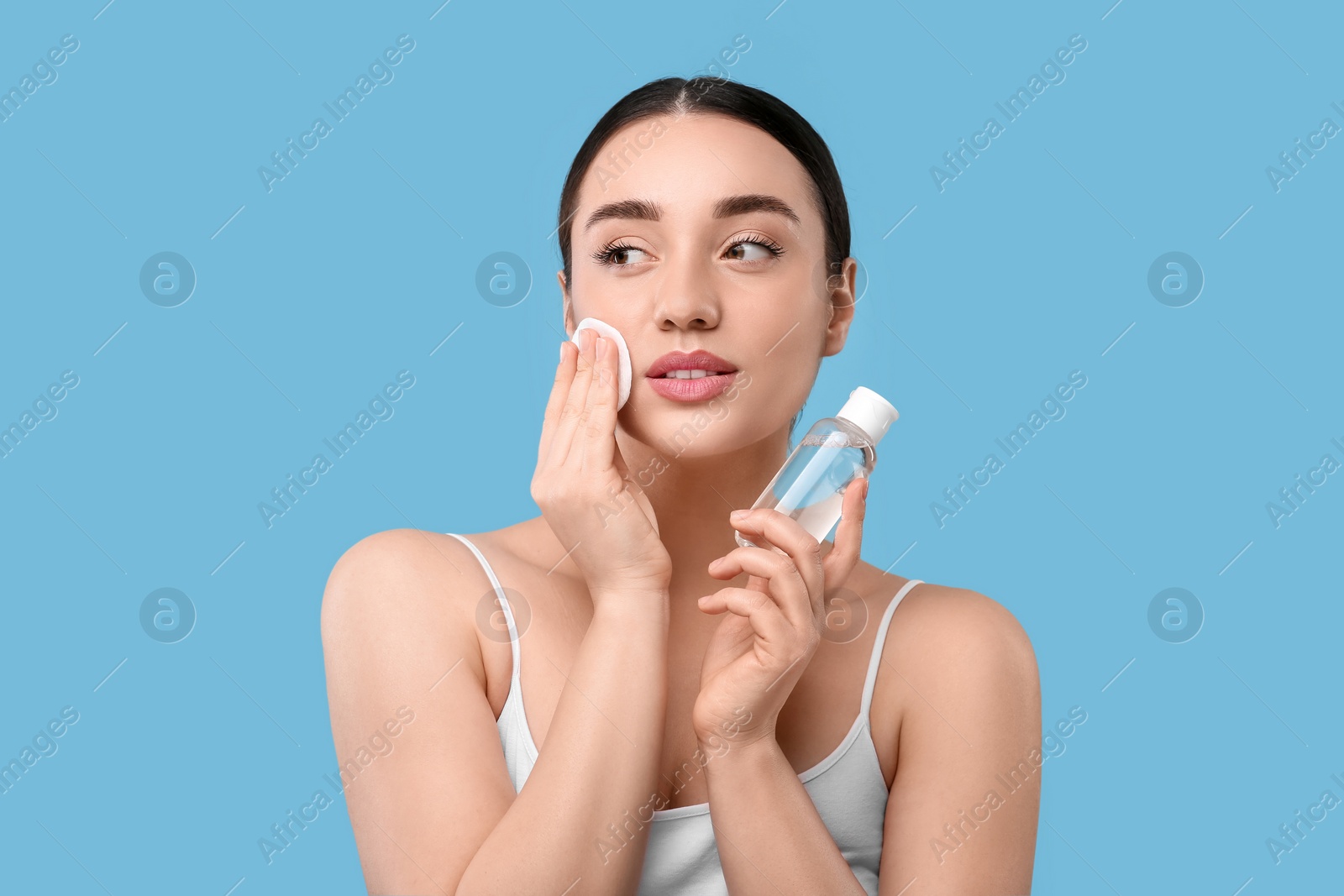 Photo of Beautiful woman removing makeup with cotton pad on light blue background