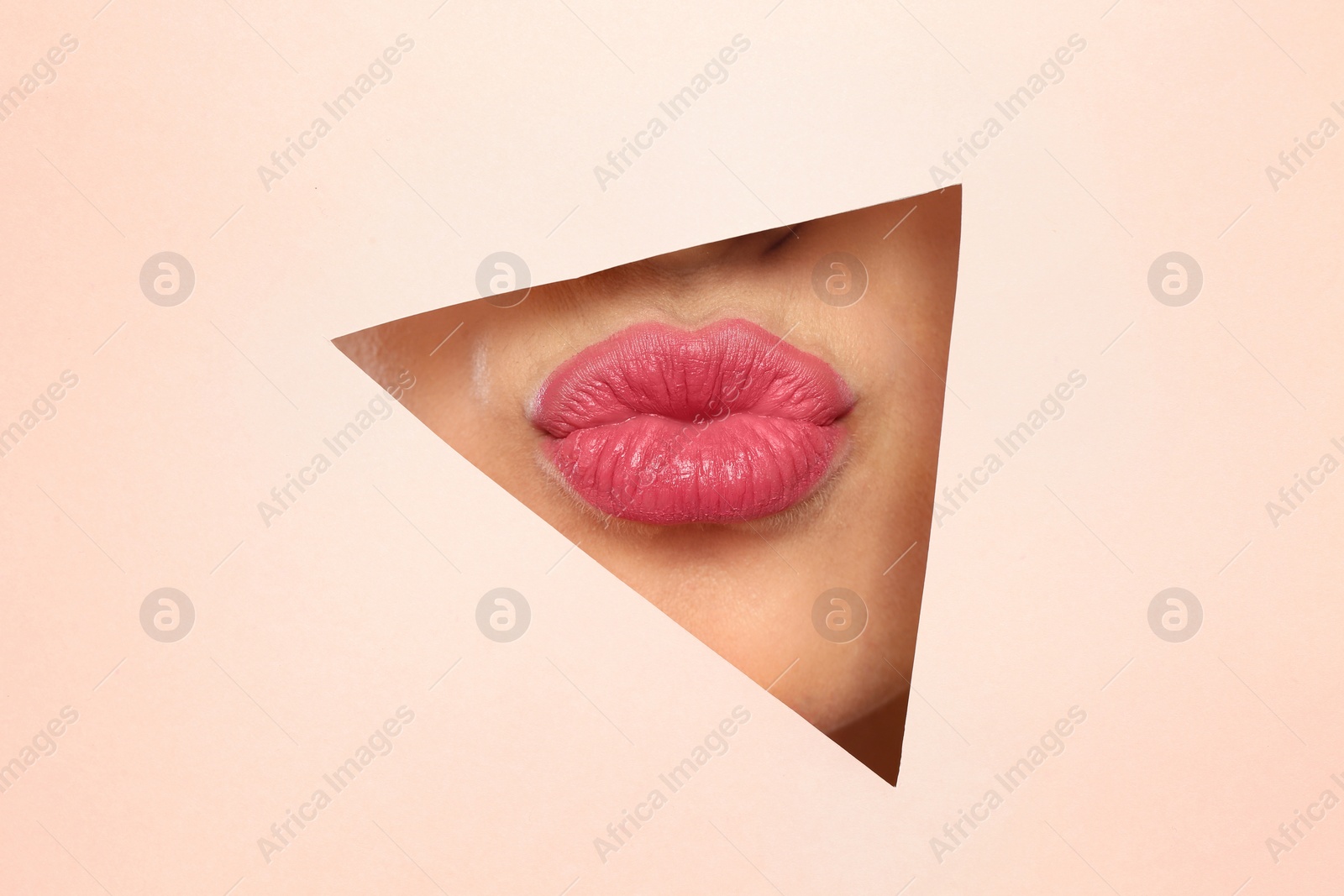 Photo of Young woman wearing beautiful lipstick, view through hole in color paper