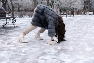 Photo of Young woman trying to stand up after falling on slippery icy pavement in park