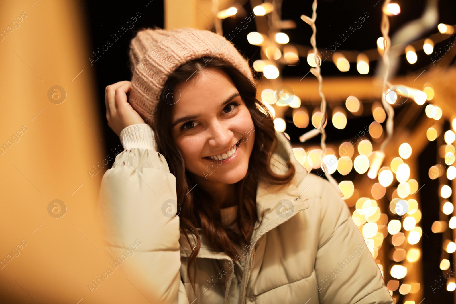 Photo of Beautiful young woman near festive lights outdoors. Winter vacation