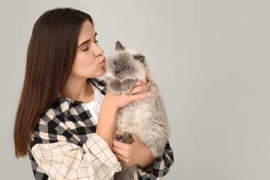 Woman kissing her cute cat on light grey background, space for text